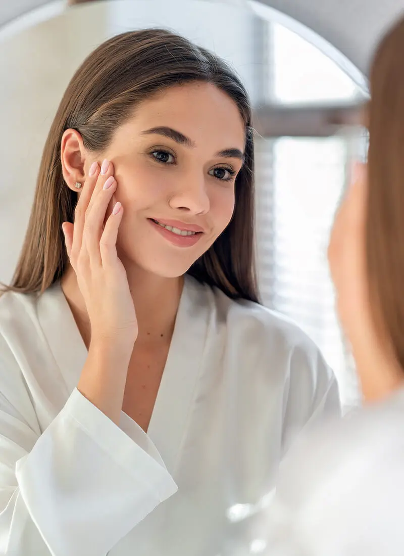 Woman looking in the mirror and touching her face